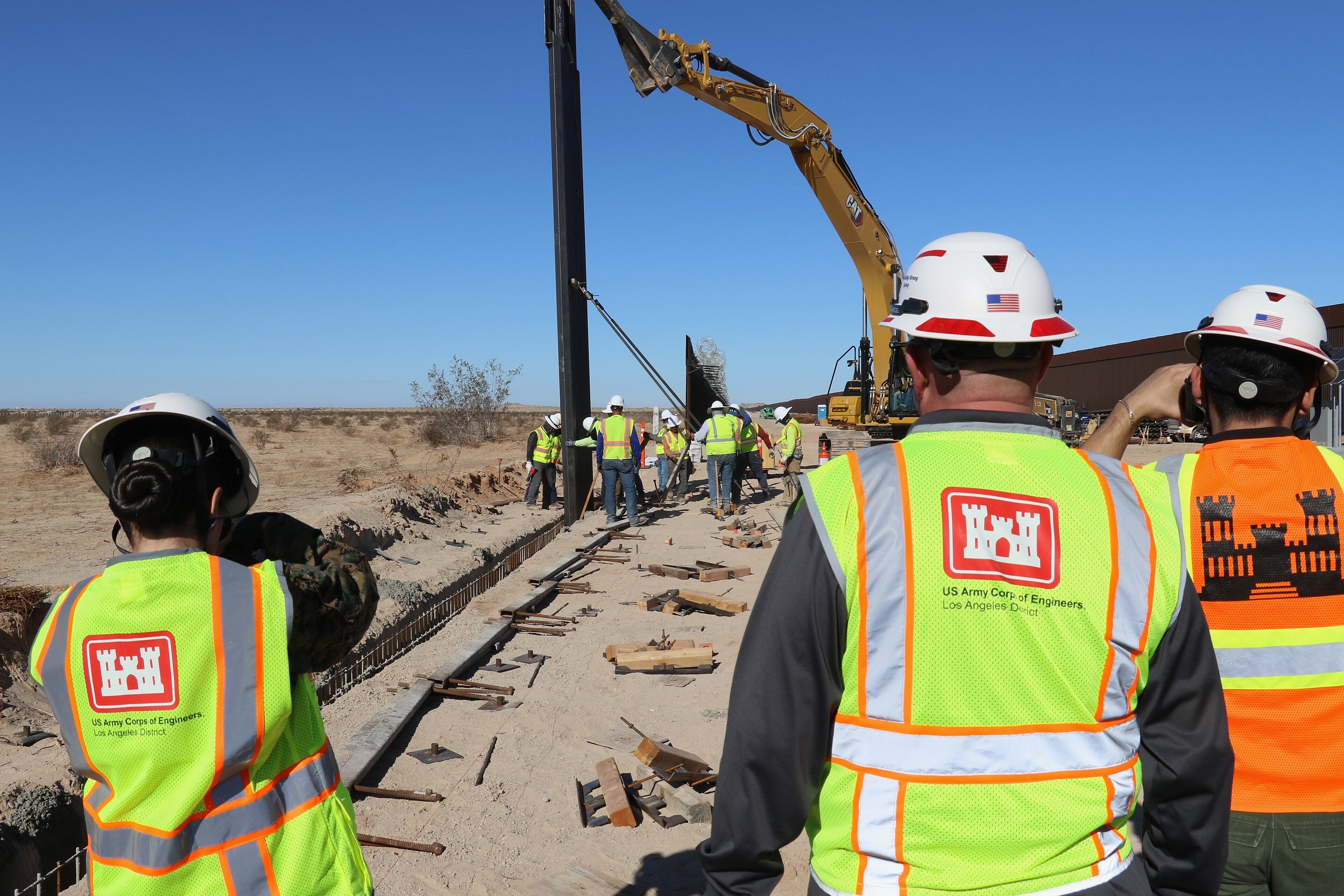 A crane lifting a steel border barrier panel into place in the Arizona desert