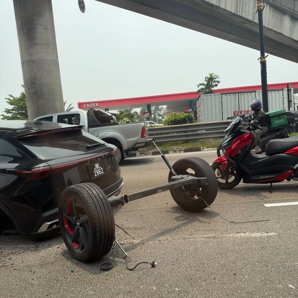 A black Chery SUV stopped on a Malaysian road under a flyover, its whole rear axle and both back wheels lying on the tar beside it