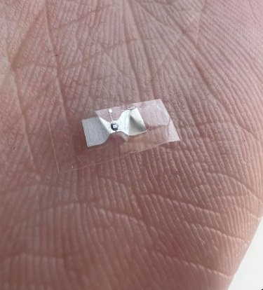 The tiny silver chip under clear tape, shown on a fingertip