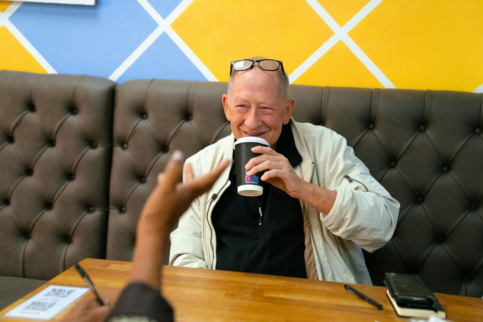 Older man smiling while drinking coffee at a cafe table