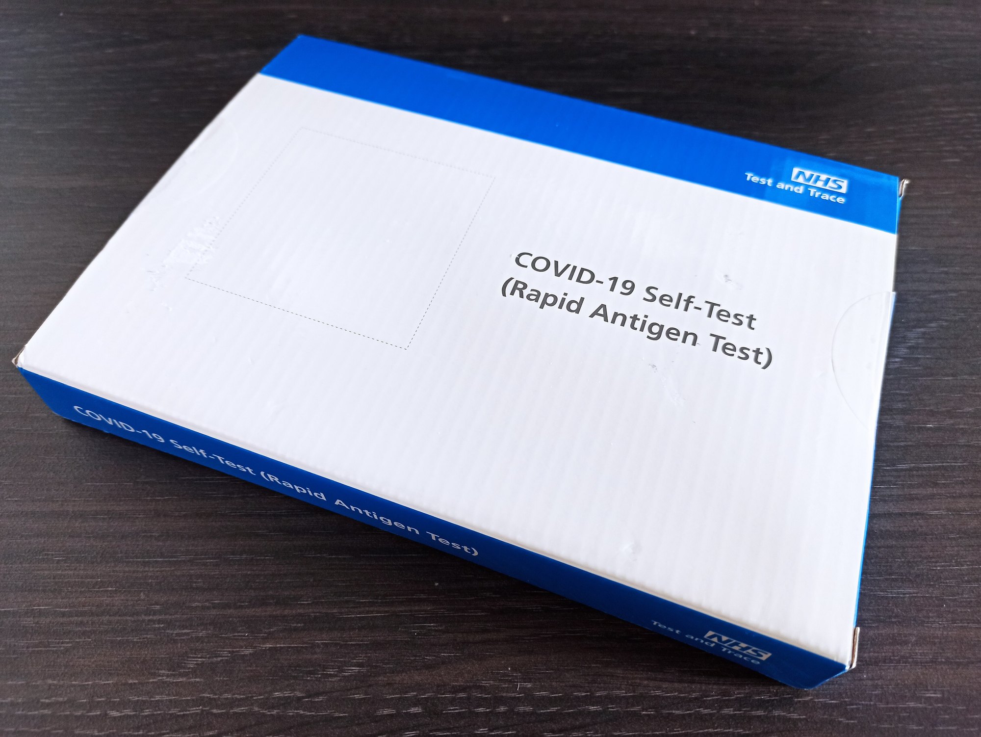 A box of NHS Covid-19 rapid self-test kits on a wooden table