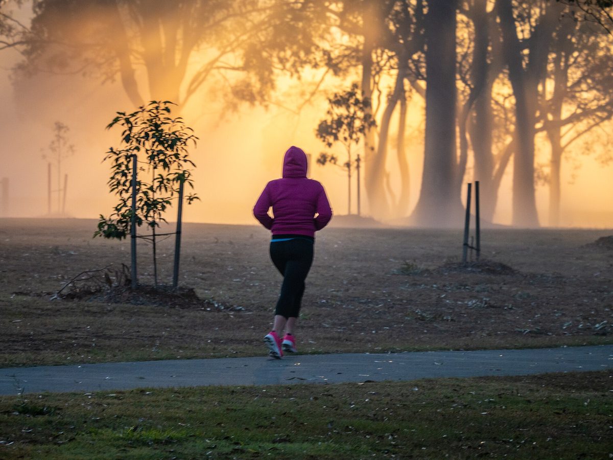 A jogger in a pink hoodie running through a misty park at sunrise