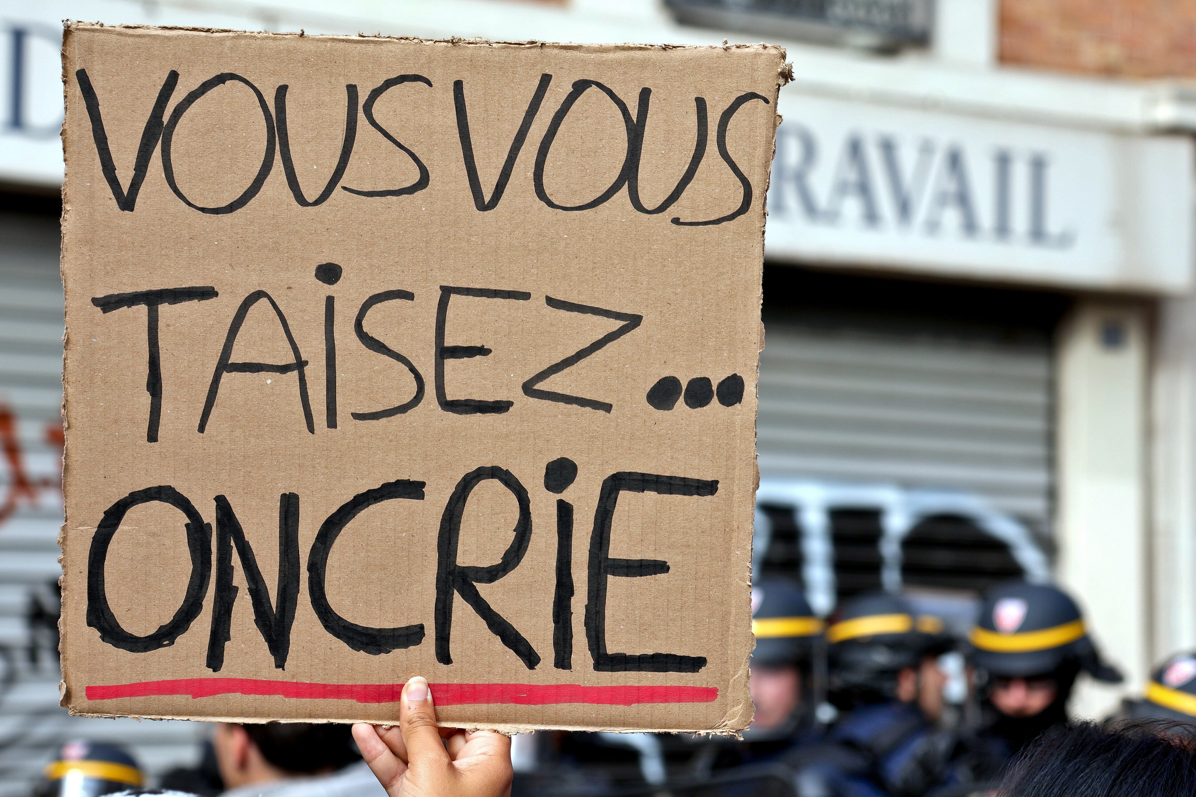 A protest sign reading Vous vous taisez, on crie held up near riot police in Paris