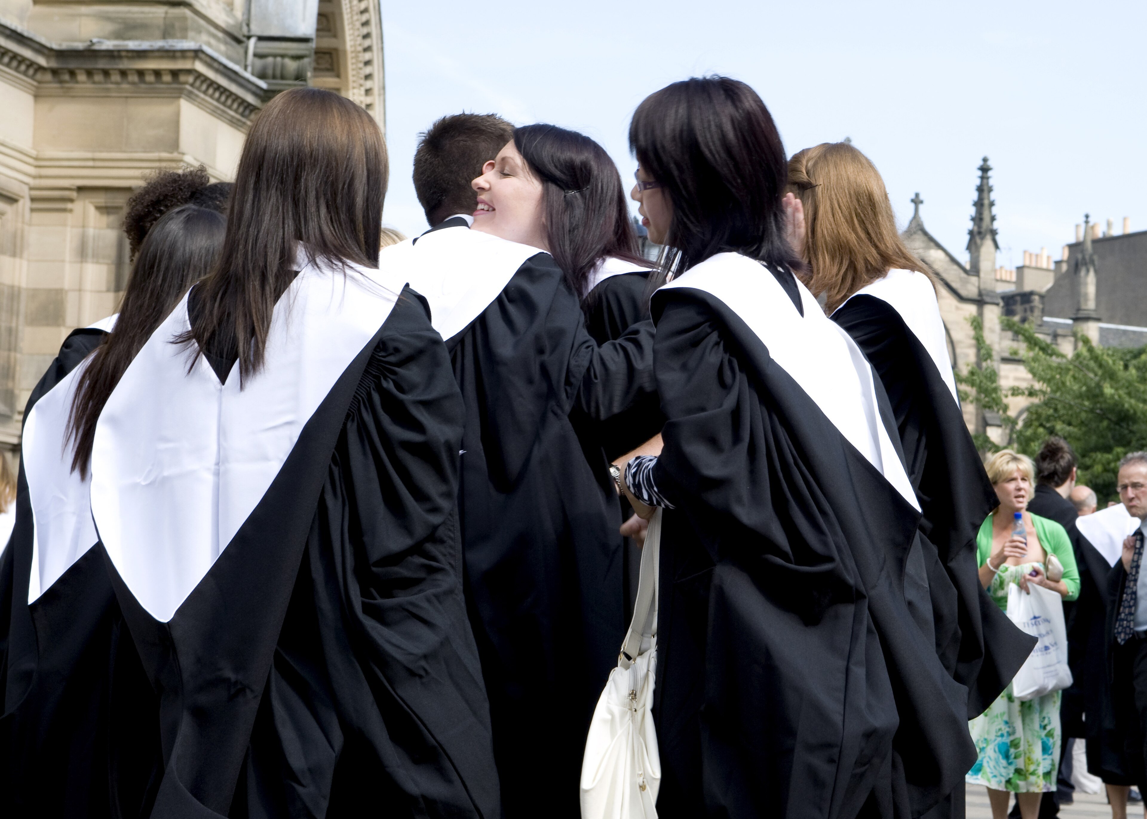 University graduates in black caps and gowns celebrate outside after their ceremony