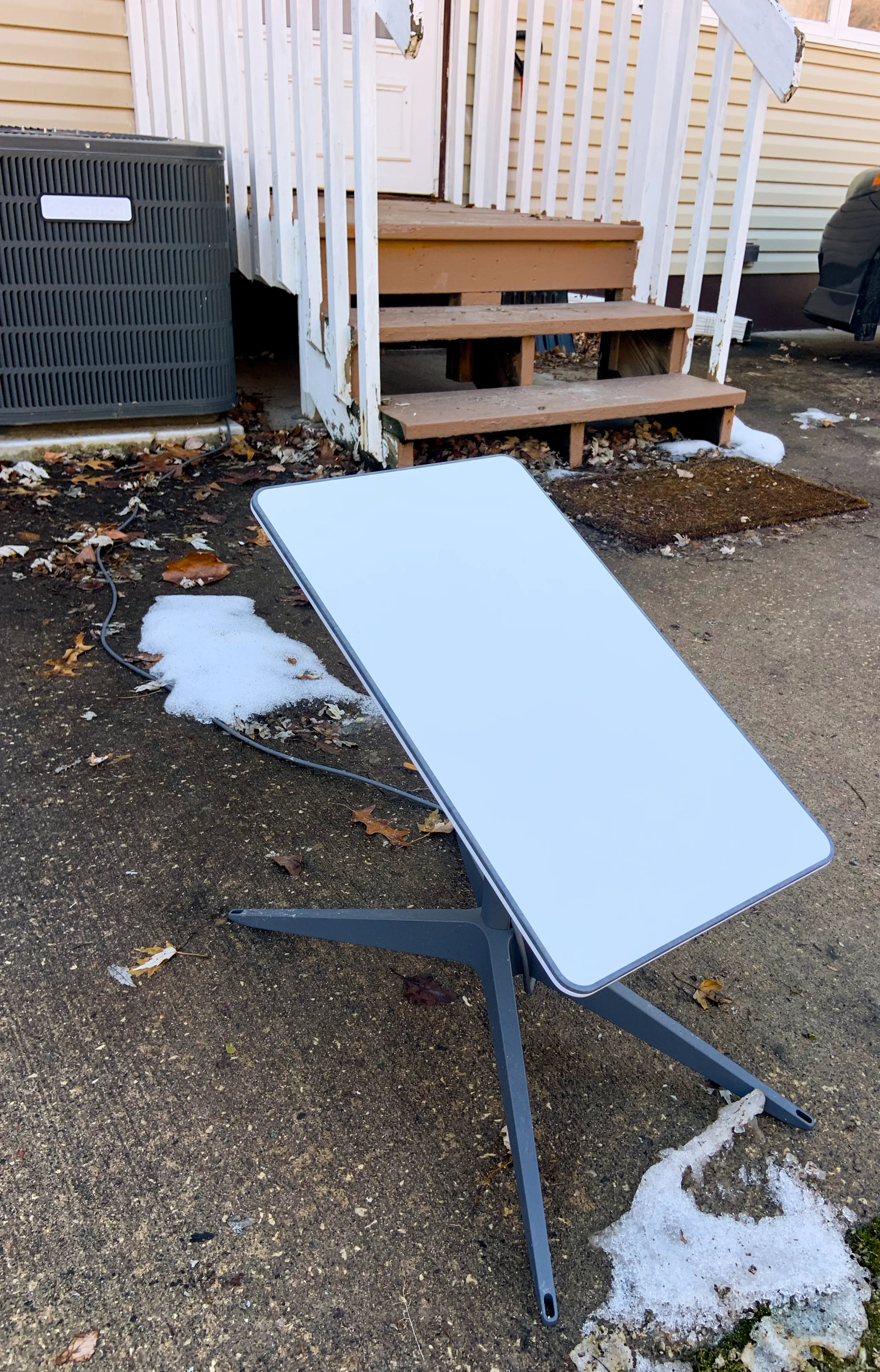 A Starlink dish set up on the ground beside a house