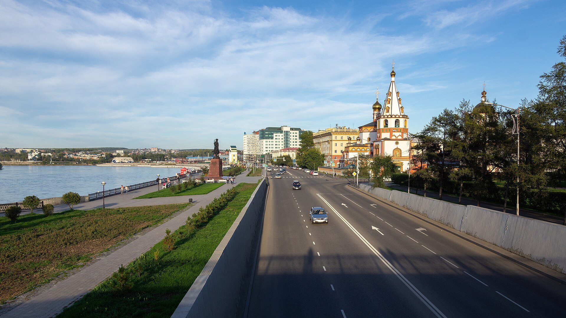 The Angara River embankment in Irkutsk on a sunny day, with the golden domes of the Epiphany Cathedral beside a wide road