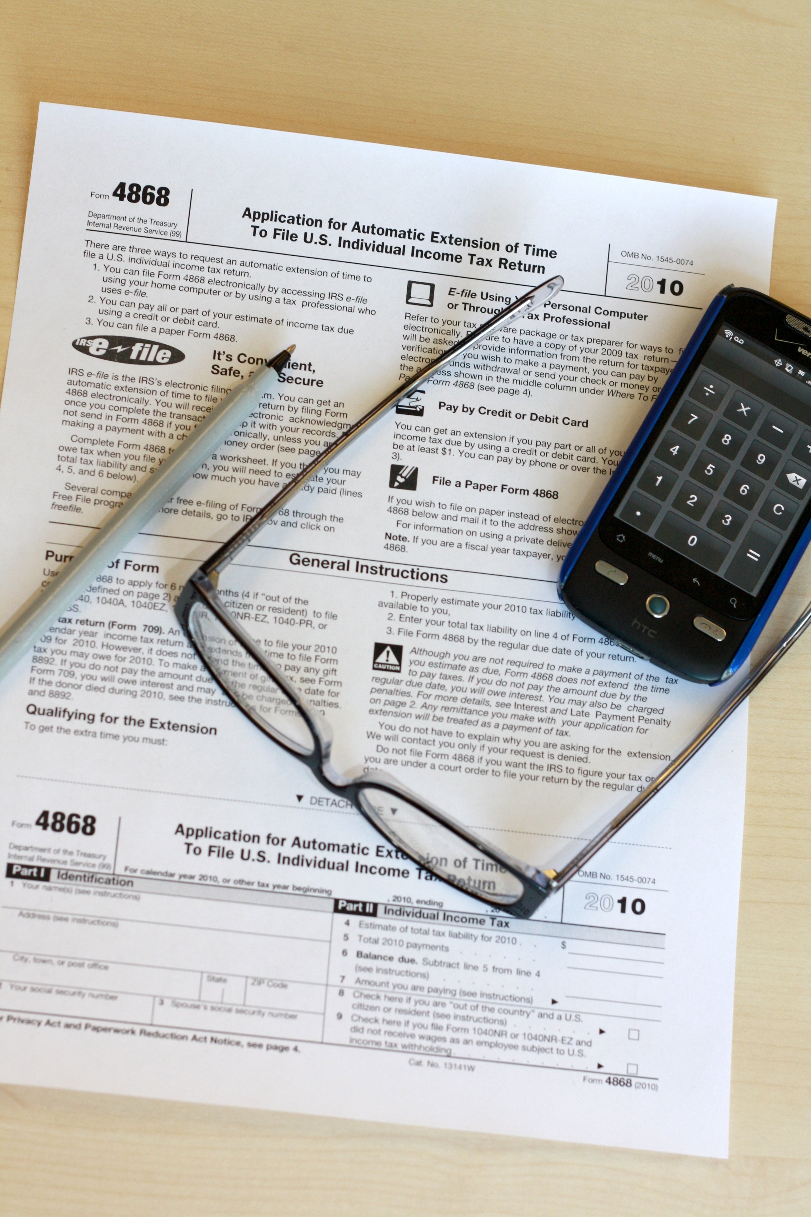 A taxpayer with glasses, a pen and a phone beside IRS Form 4868, the extension form