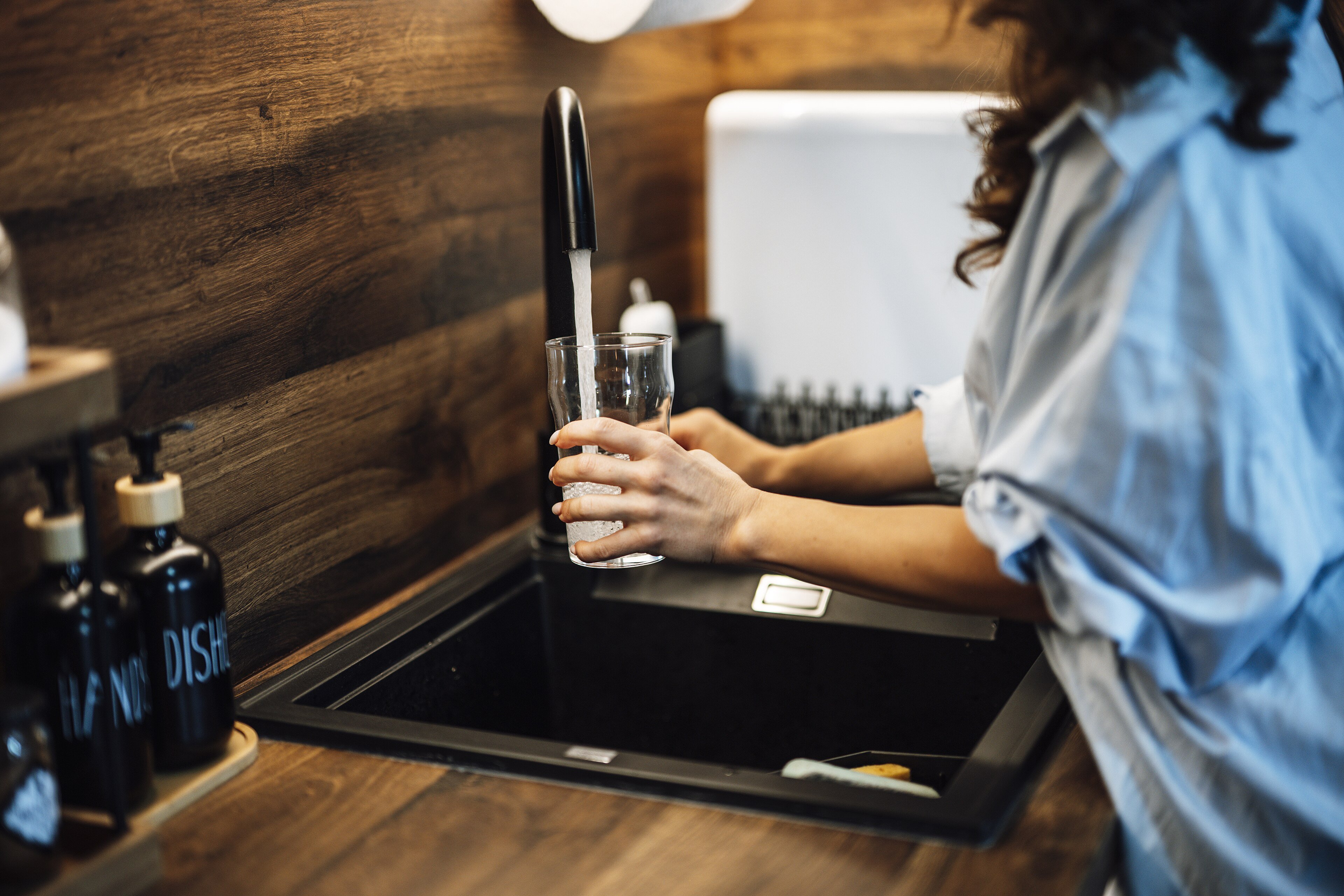 A person fills a glass with tap water at a kitchen sink