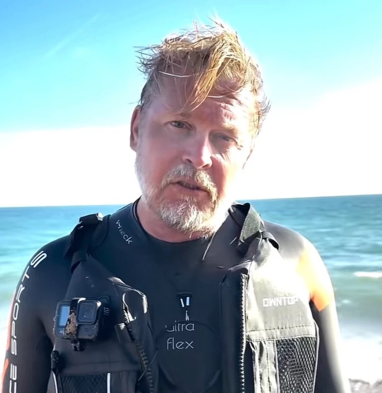 Karl Bushby with a grey beard and wet hair in a wetsuit on the beach after swimming the Channel
