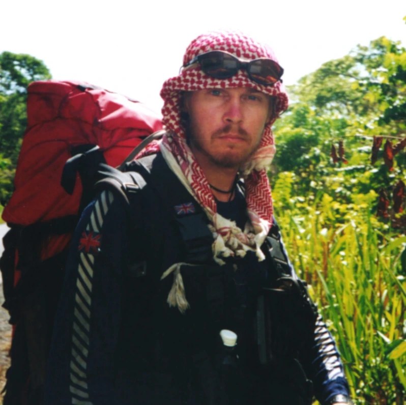 Young Karl Bushby in a red and white keffiyeh with a heavy backpack early in his walk