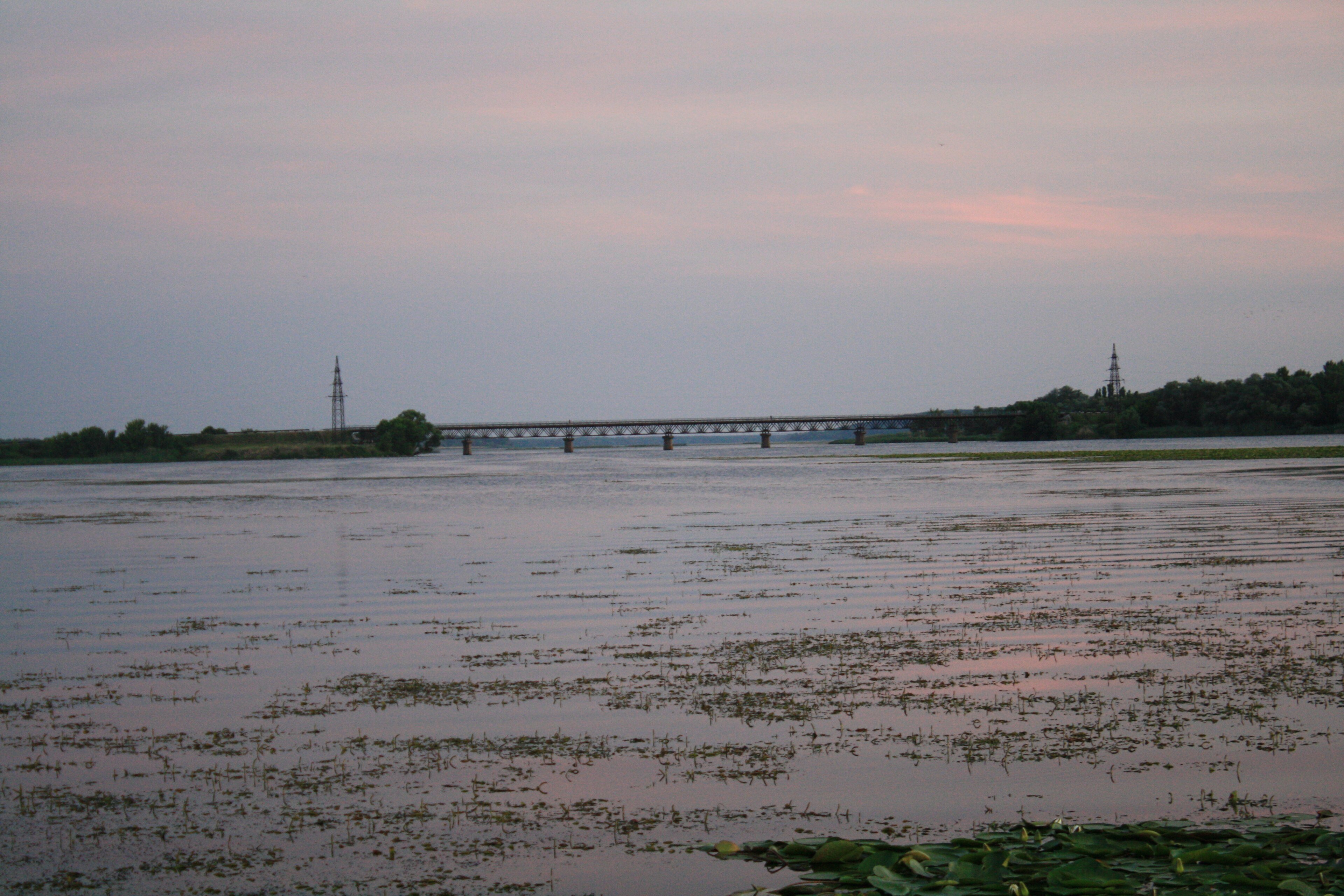 The Oskil River in Kharkiv Oblast at dusk, with a long rail bridge crossing the water