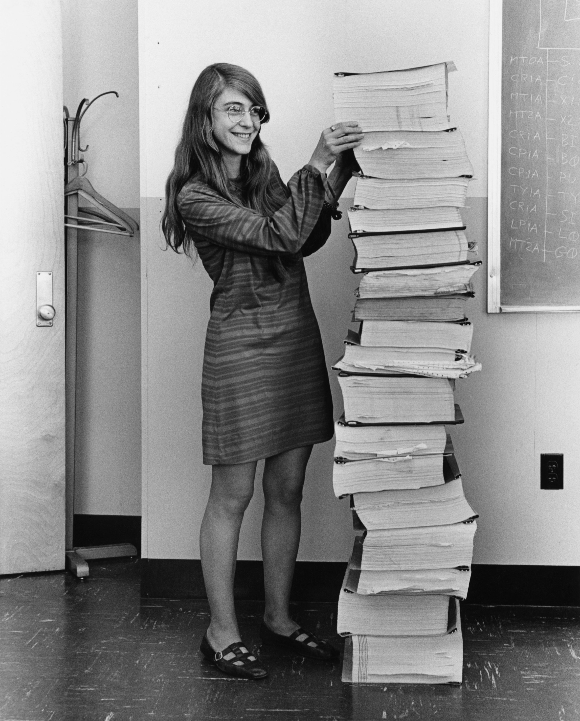 Margaret Hamilton in 1969 standing beside a stack of printed Apollo guidance software listings as tall as she is