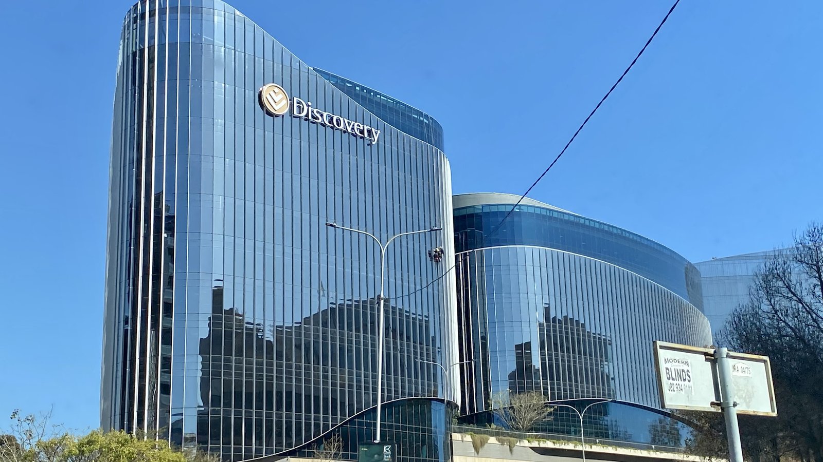 Discovery's glass head office building in Sandton under a blue sky