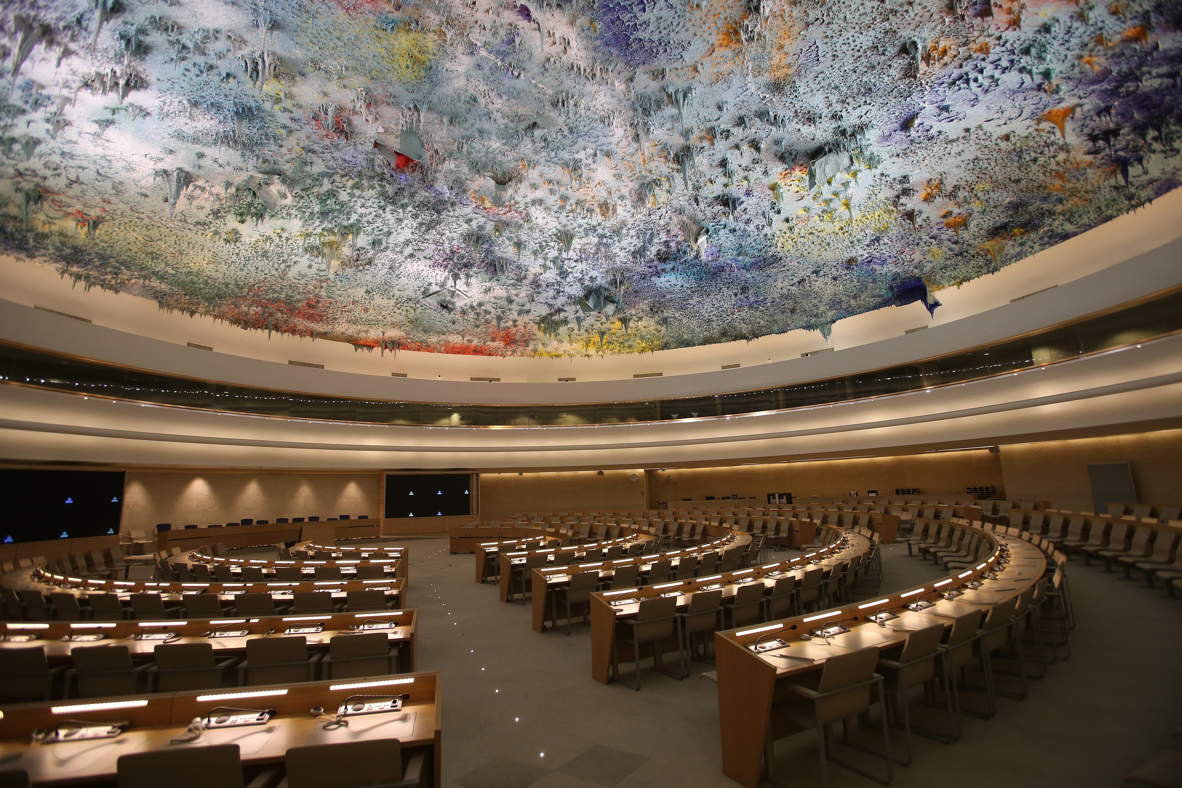 The Human Rights Council chamber in Geneva, with rows of delegate desks under a ceiling painted in swirls of colour