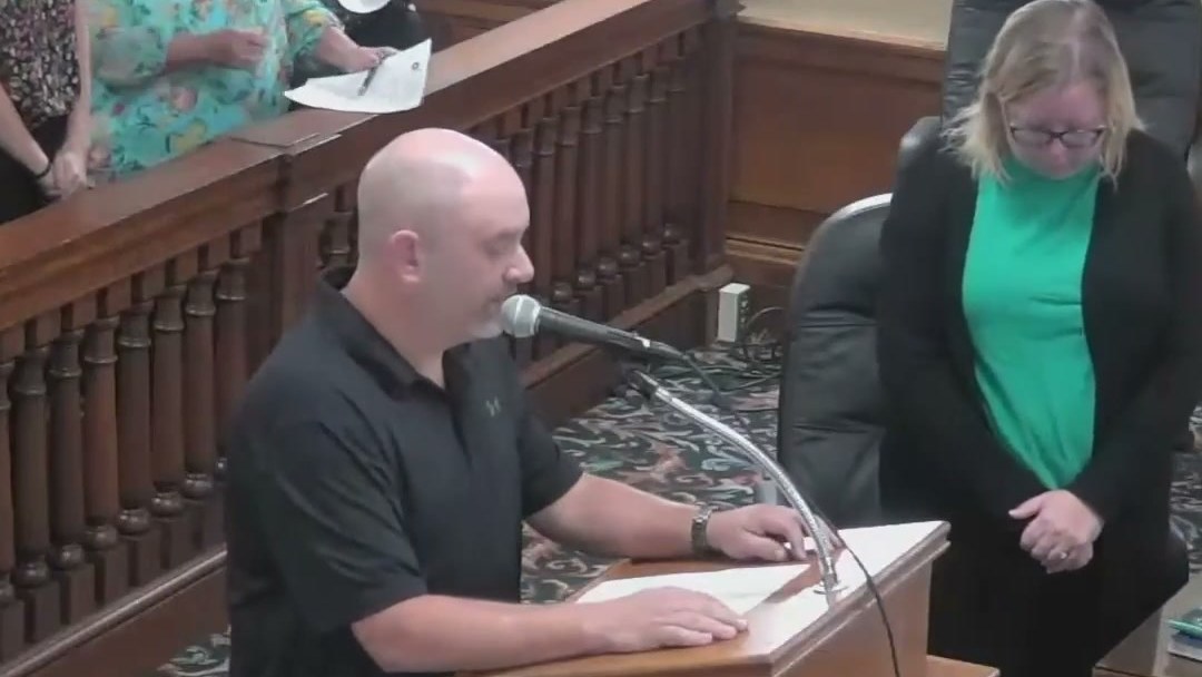 A speaker at the lectern during the invocation at the Ottumwa City Council meeting in Iowa, with residents standing behind