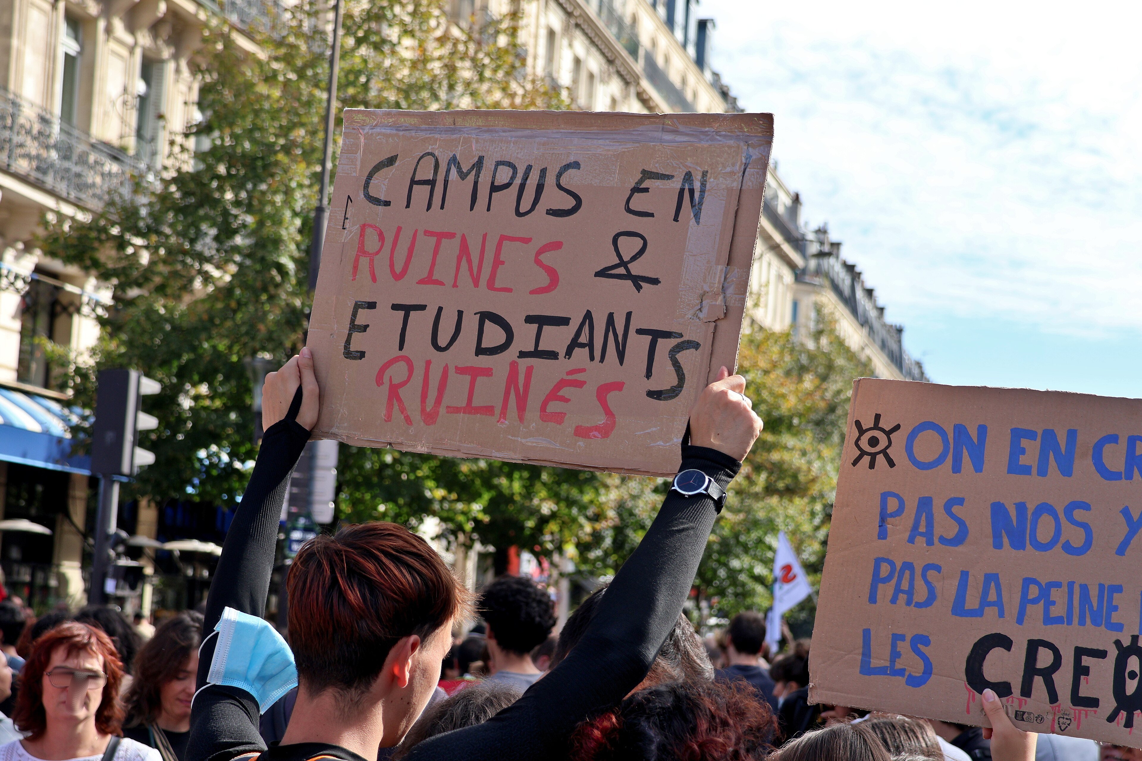 Students in a Paris crowd hold up a cardboard sign reading Campus en ruines et étudiants ruinés during the 6 October 2026 march