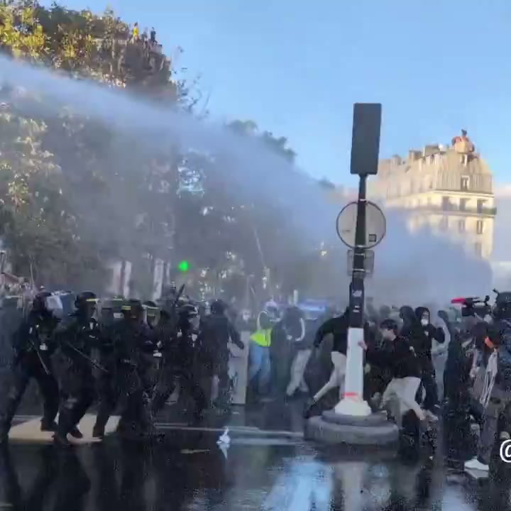 Riot police and a water cannon push back a crowd on a wet Paris square