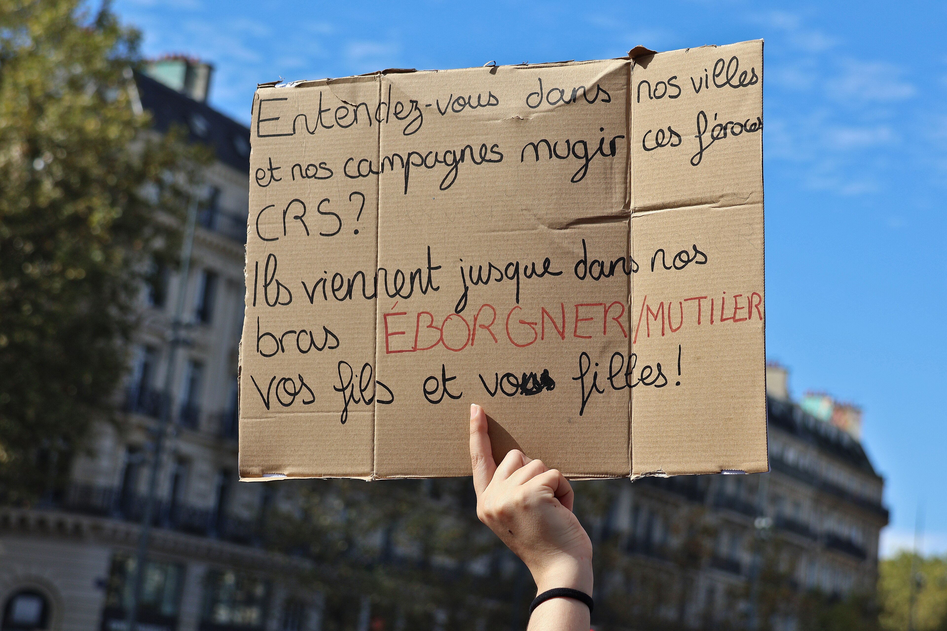 A handwritten protest sign held up against a blue sky in Paris
