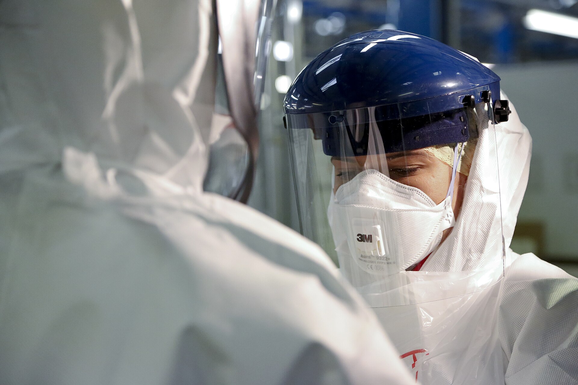 A medic in a face shield, respirator mask and full white protective suit