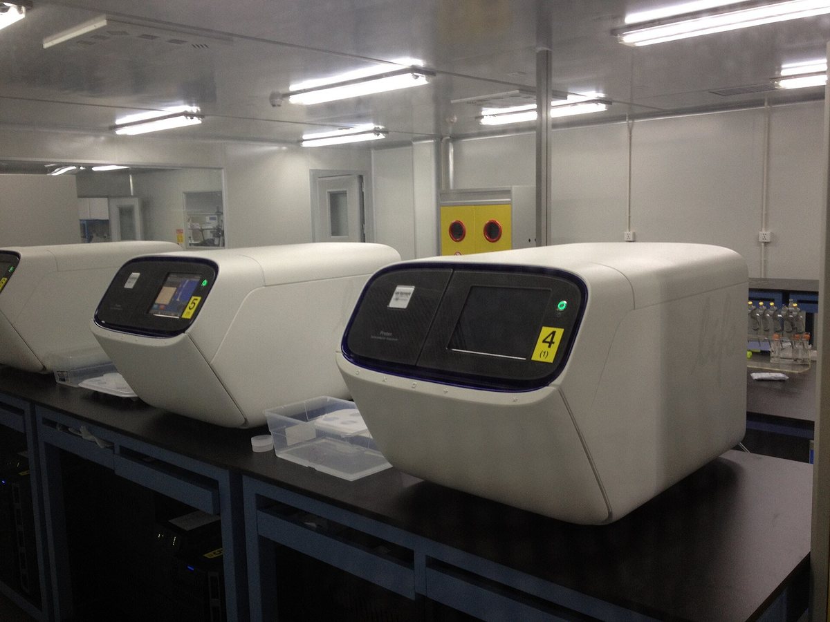 Several white DNA sequencing machines lined up on benches in a bright laboratory