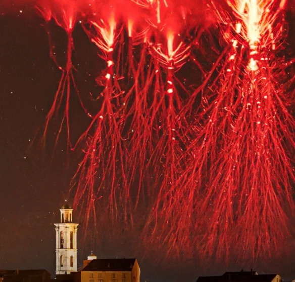 A cluster of giant red jellyfish-shaped sprites glowing above a lit church bell tower at night