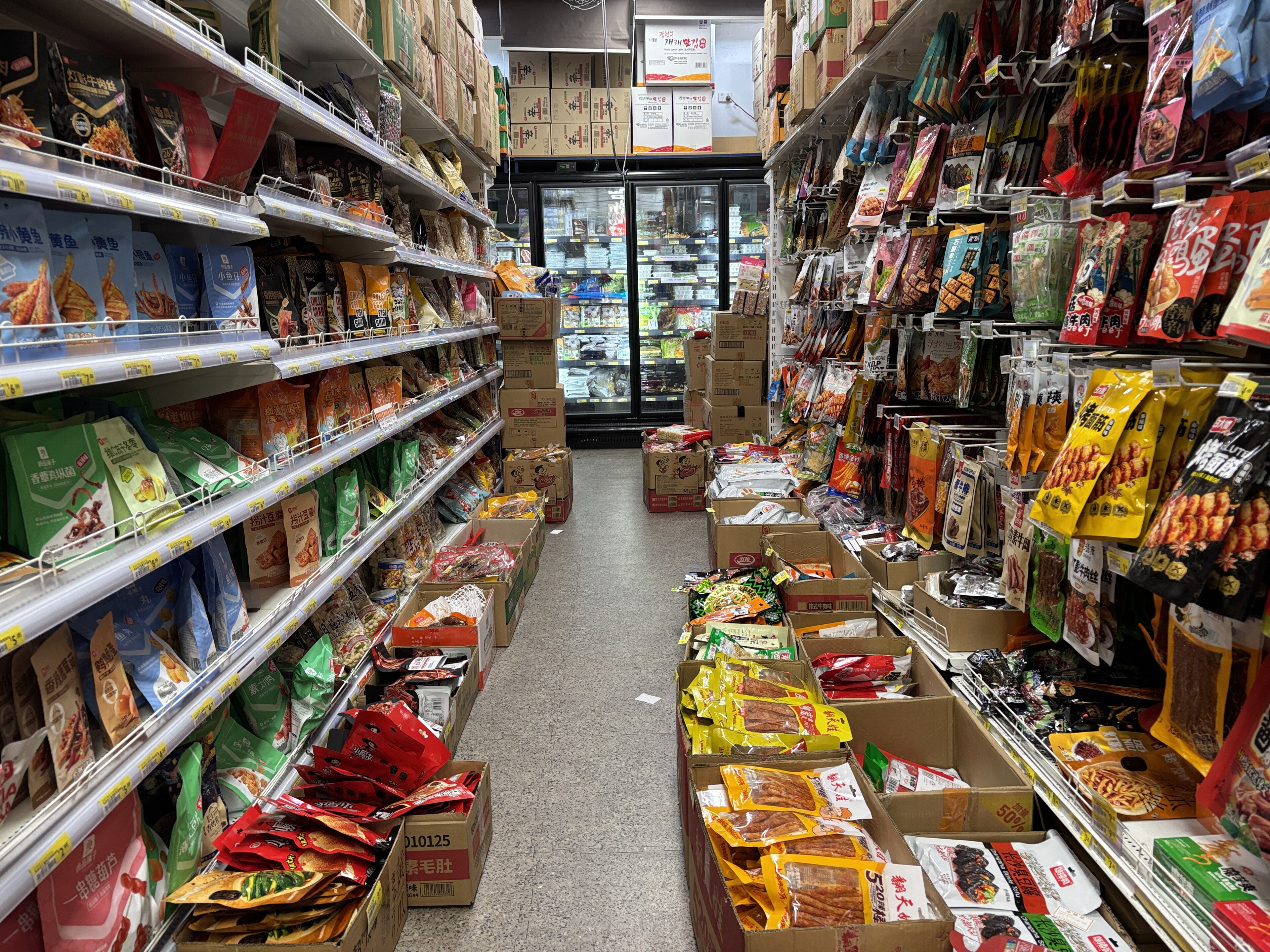 A supermarket aisle stocked with shelved groceries and price tags