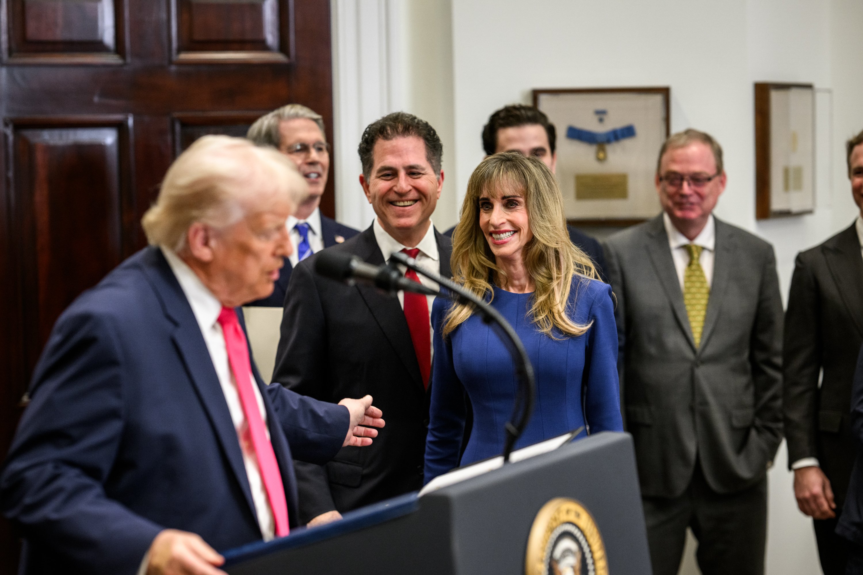Michael and Susan Dell smile beside Donald Trump at a White House lectern during the Trump Accounts gift announcement