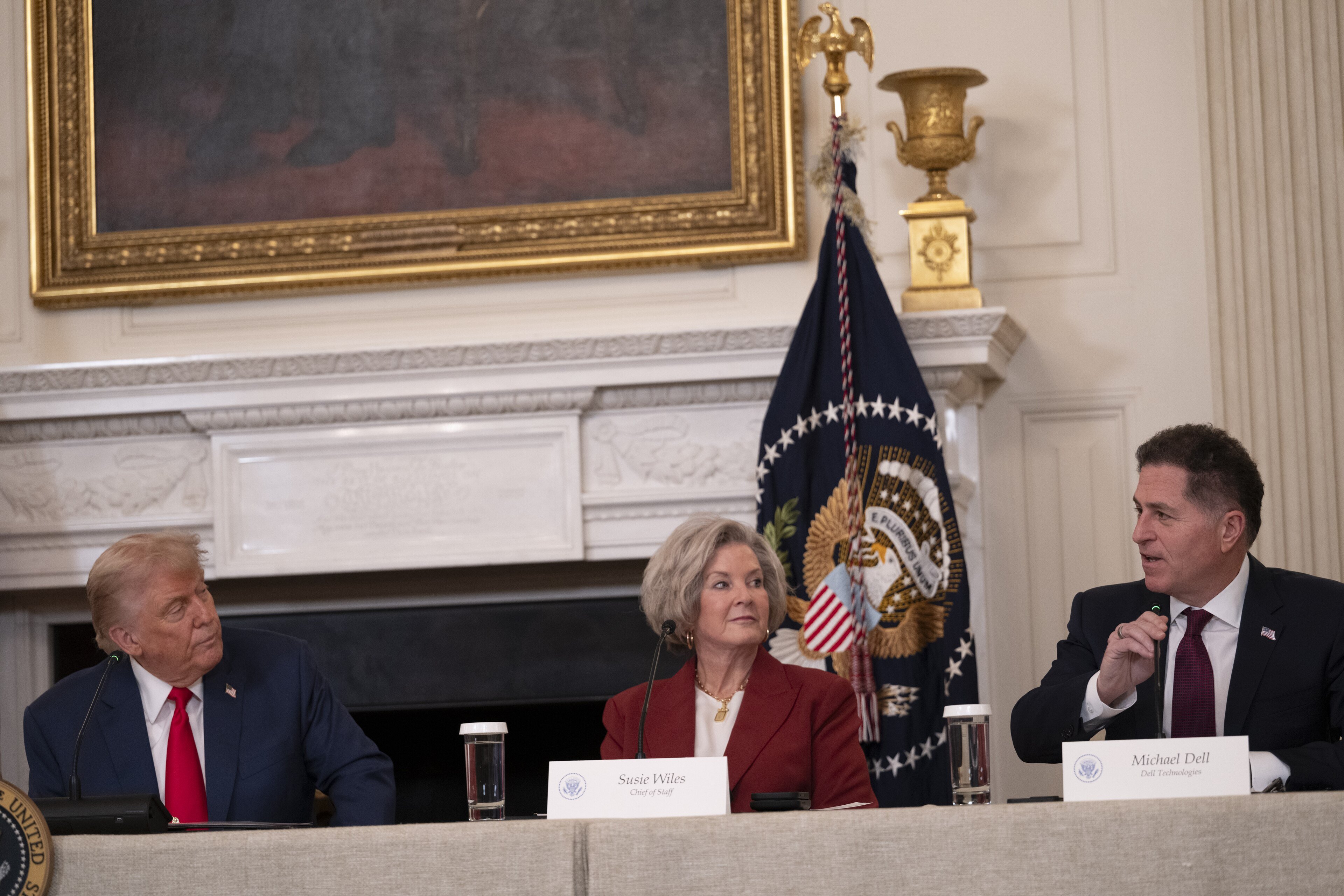 Michael Dell speaks at a long table in the White House State Dining Room, with Donald Trump and Susie Wiles beside him