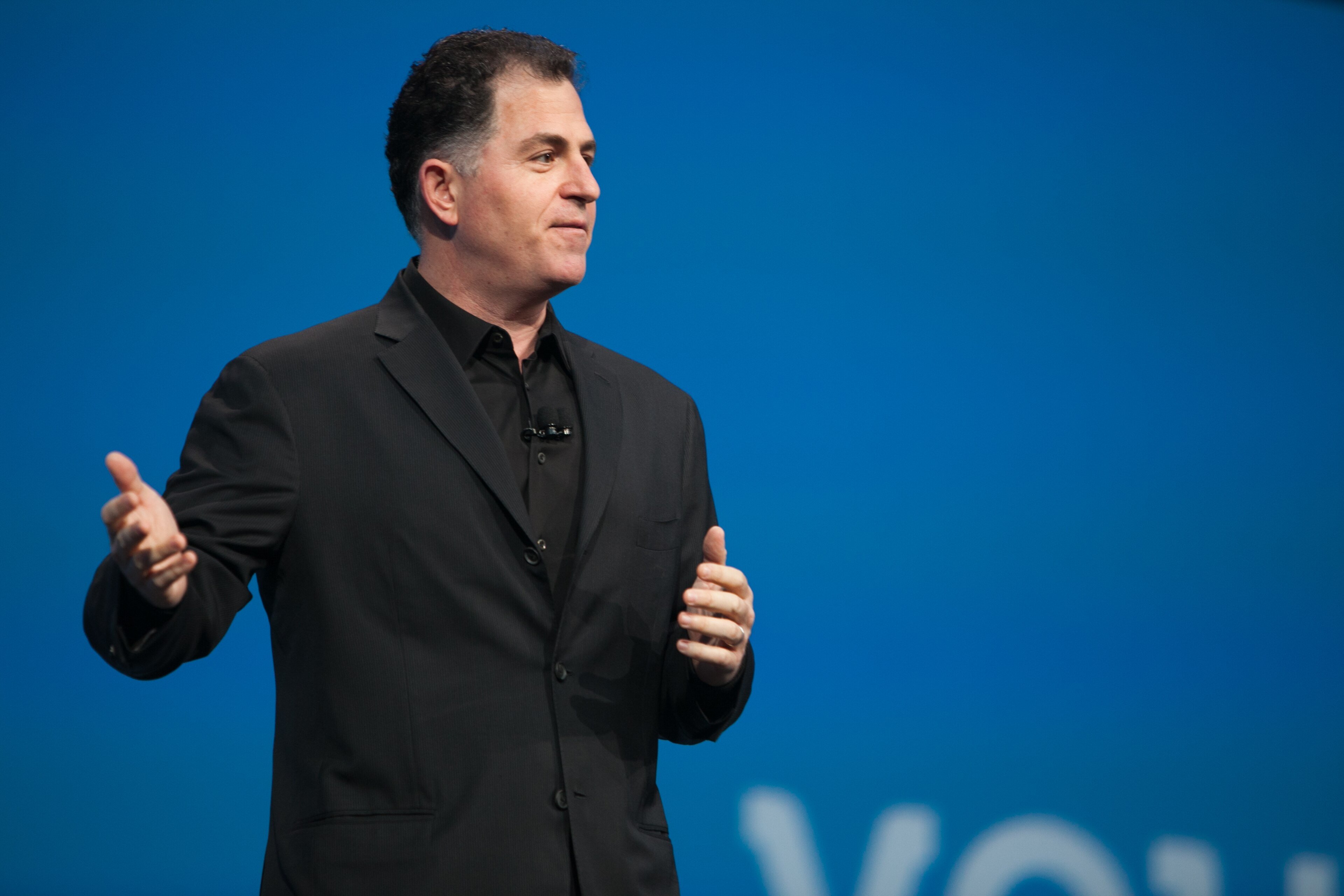 Michael Dell on stage in a dark suit, speaking into a microphone