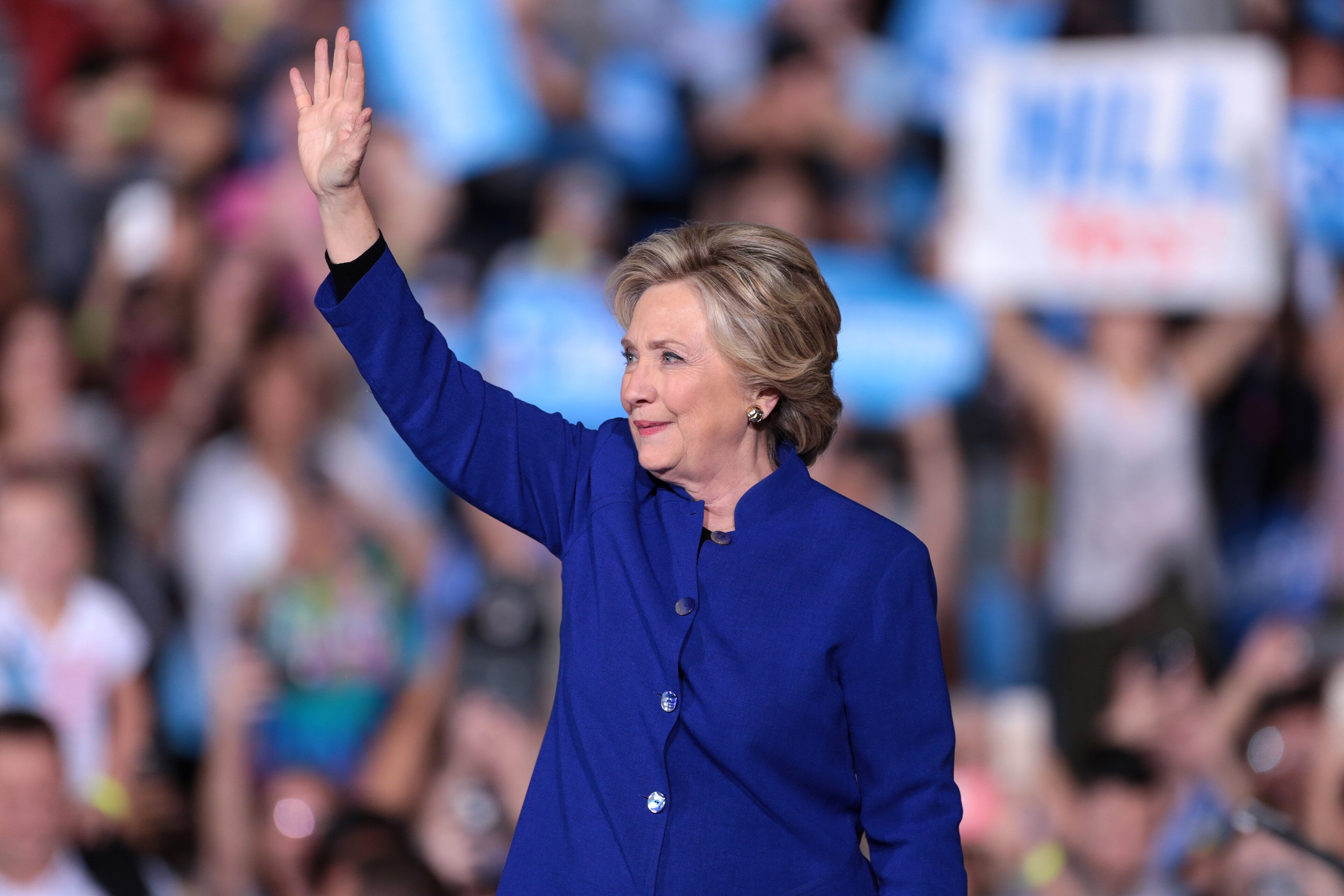 Hillary Clinton smiles and waves to a crowd at an outdoor campaign rally
