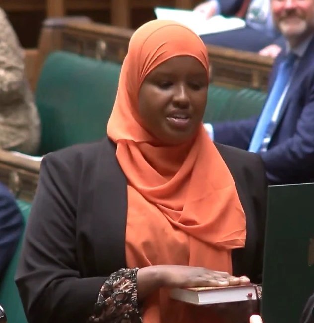 Sagal Abdi-Wali, wearing an orange hijab, takes her oath in the House of Commons with her hand on the Quran