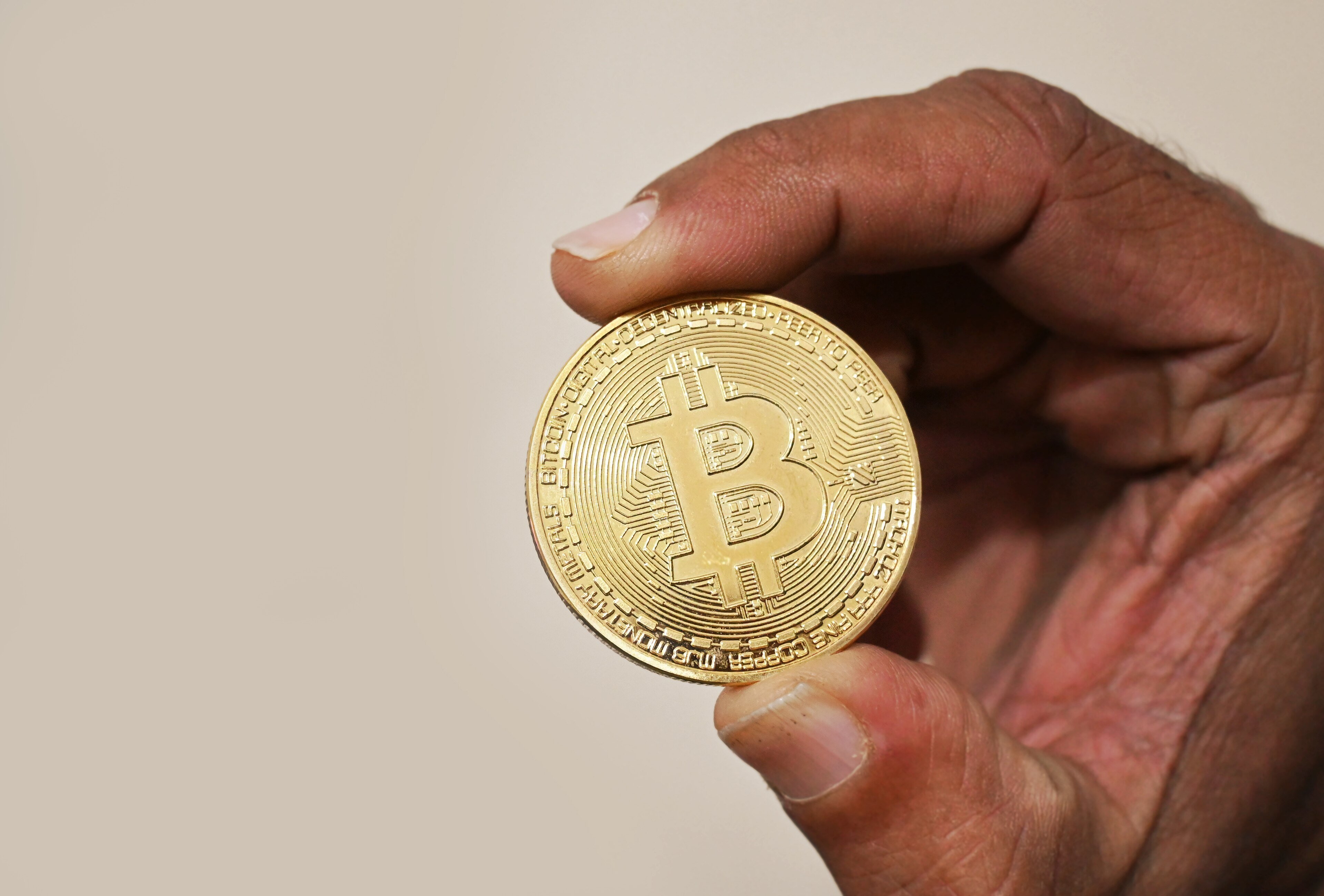 A hand holding a gold bitcoin coin up to the light