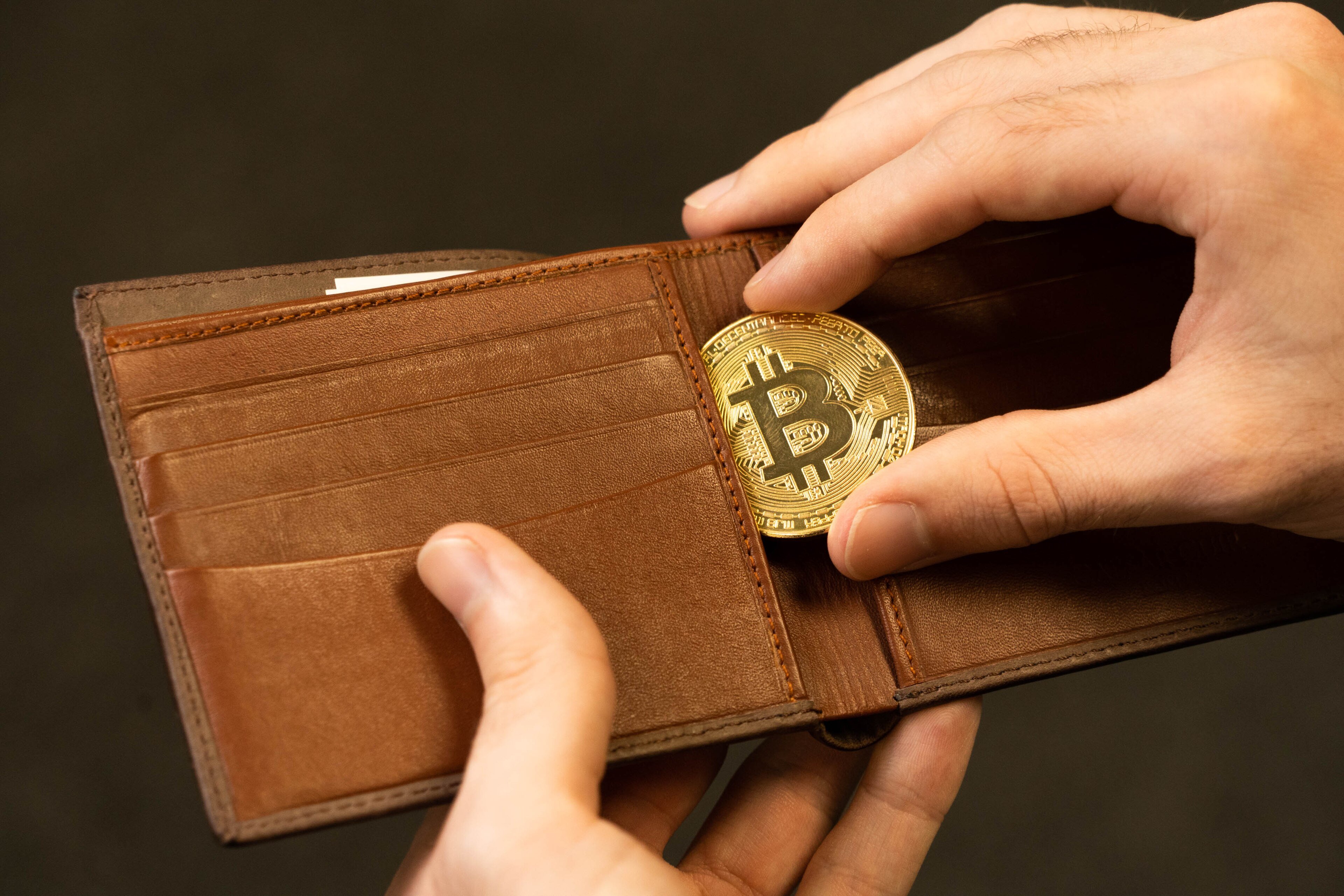 A gold bitcoin medallion going into a leather wallet
