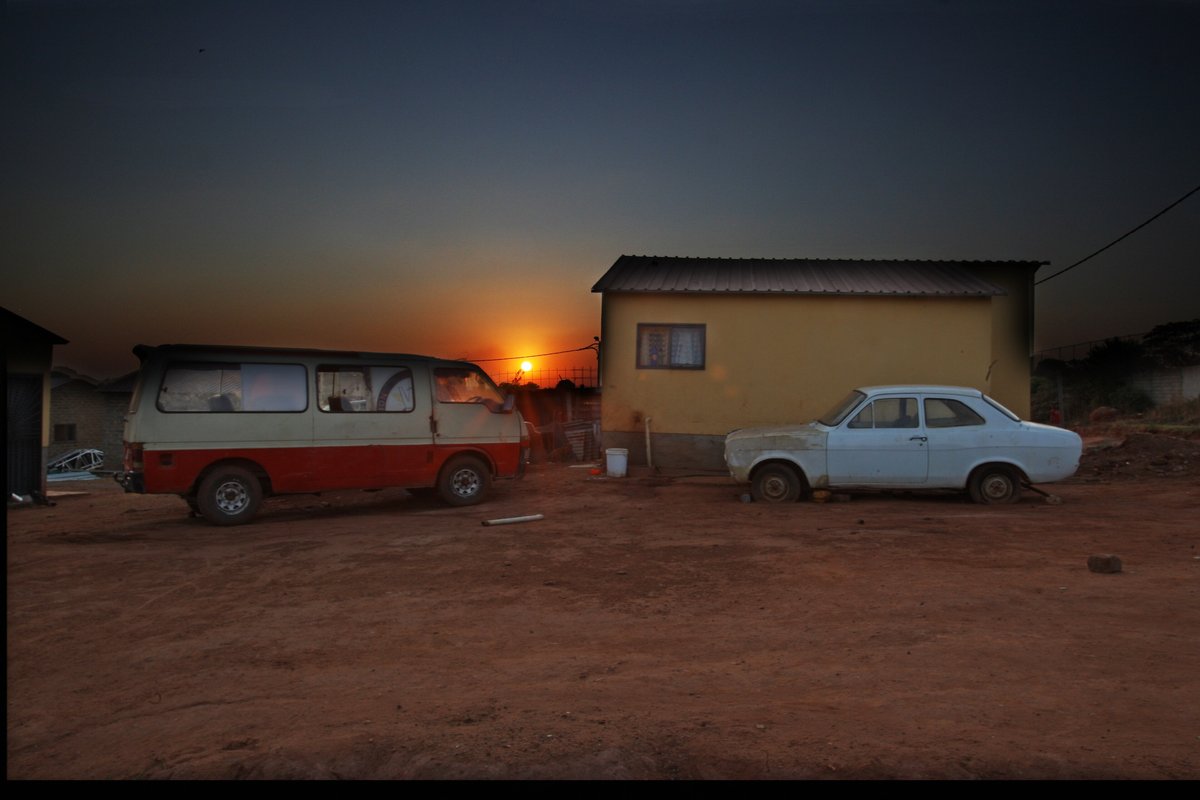 A minibus taxi and an old car parked outside a house in Soweto at sunset